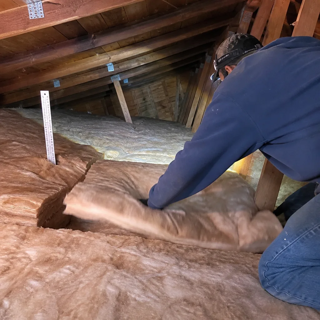 Technician installing attic fiberglass batt insulation in a residential roof space
